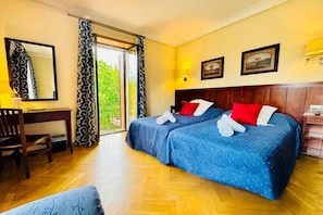 Hotellihuone, jossa on kaksi sänkyä, työpöytä, tuoli, suuri peili ja liukuovi, joka johtaa ulos.