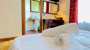 Ein Hotelzimmer mit Bett, Schreibtisch, Stuhl, Lampe und einem durch eine offene Tür einsehbaren Badezimmer.