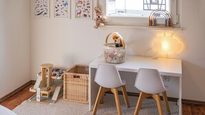 Un espace de jeu pour enfants comprenant un bureau, deux chaises, un panier et une voiture jouet.
