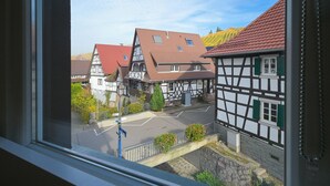 Une maison traditionnelle à colombages, avec un toit rouge, visible à travers une fenêtre.