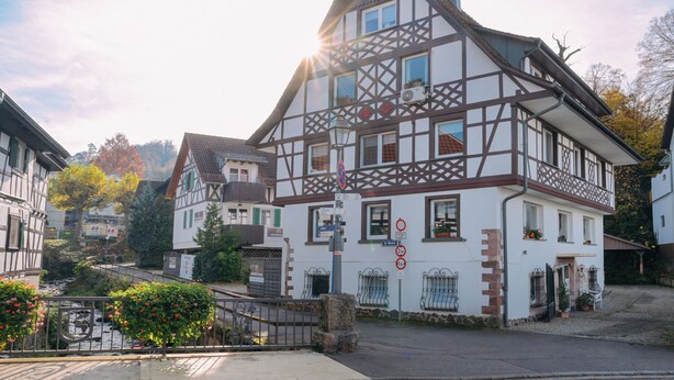 Un bâtiment traditionnel à colombages, doté d’un balcon, d’un petit jardin et d’un pont piétonnier.
