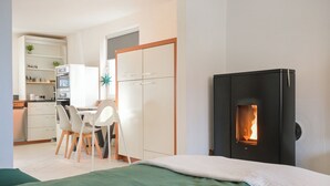 Une chambre avec un lit, une petite kitchenette, un coin repas avec des chaises et un poêle à bois.