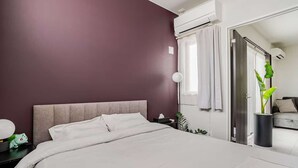A modern bedroom with a large bed, a nightstand, a lamp, and a potted plant. - New Luxury Home in Koza | Work-Friendly | Free Parking (沖縄県)