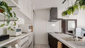 A modern kitchen with white cabinetry, a microwave, a stove, and a hanging plant. - New Luxury Home in Koza | Work-Friendly | Free Parking (沖縄県)