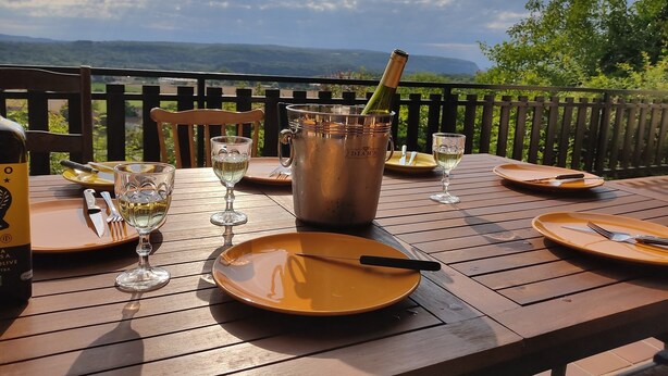 A dining table set outdoors with wine glasses, a bottle, and a metal bucket. - Chez Sam - Bed & Breakfast (Villebois)