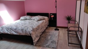 A bedroom with a bed, a nightstand, a floor lamp, a hanging plant, and a coat rack. - Chez Sam - Bed & Breakfast (Villebois)