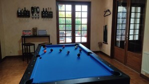 A pool table with balls, a bar area with bottles, and a view through a door. - Chez Sam - Bed & Breakfast (Villebois)
