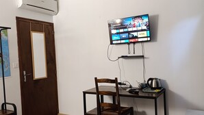 A room with a bed, a desk with a chair, a television mounted on the wall, and an air conditioning unit. - Chez Sam - Bed & Breakfast (Villebois)