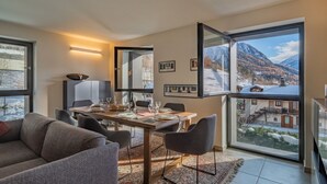 A modern living room with a dining area, large windows with a mountain view, and a cozy fireplace. - MAISON GLENDA - Breathe in the alpine stillness (Courmayeur)