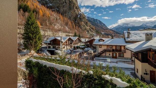 A mountain village with traditional wooden houses, a snow-covered landscape, and a prominent rocky mountain in the background. - MAISON GLENDA - Breathe in the alpine stillness (Courmayeur)