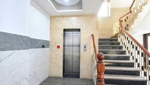 A modern elevator with a marble wall, a wooden handrail, and a staircase with a geometric design. - Hotel Vibe BLU (Noida)