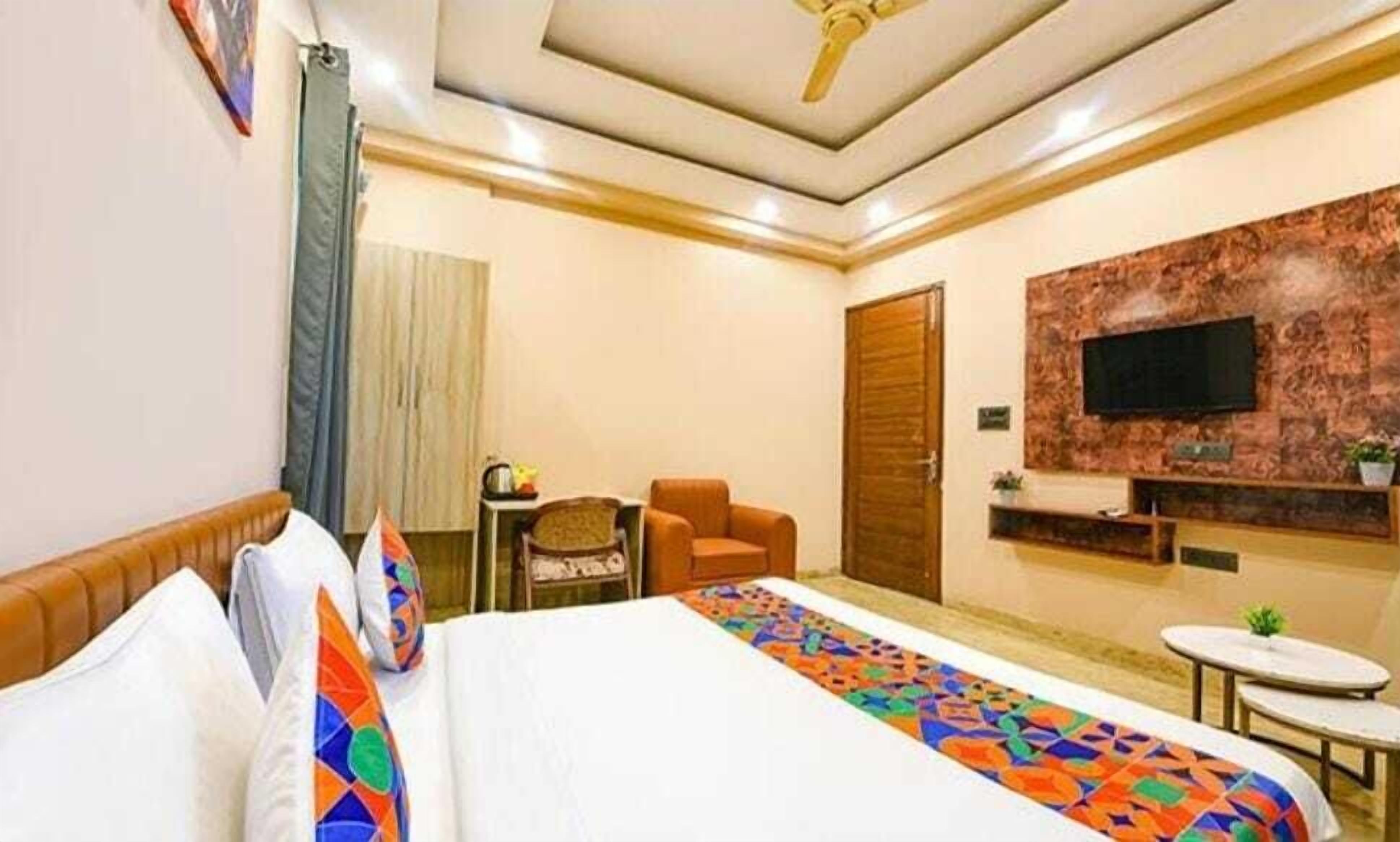 A hotel room with a bed, a desk, a chair, a TV mounted on a stone wall, and a ceiling fan.