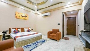 A hotel room with a bed, a chair, a TV, and a painting on the wall. - Hotel Vibe BLU (Noida)