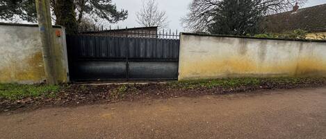 A gated entrance with a metal gate, a concrete wall, and a paved driveway.