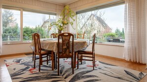 A dining area with a round table, four chairs, a chandelier, and large windows with curtains. - Holiday Home "Villa for 8 Guests – Porte du Ried" with Mountain View, Private Terrace & Wi-Fi (porte du ried)