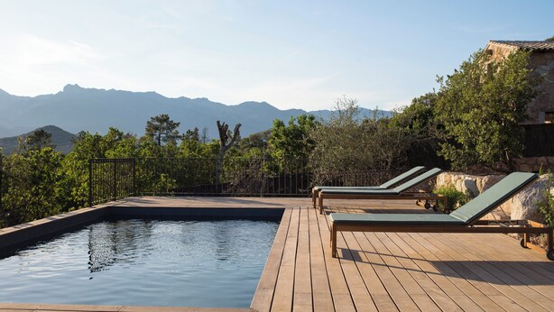 Une terrasse en bois avec une piscine, deux chaises longues et une vue sur les montagnes.