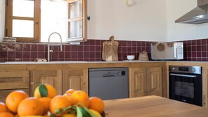 Une cuisine avec des meubles en bois, un lave-vaisselle, un four, un four à micro-ondes et une fenêtre dont les volets sont ouverts.