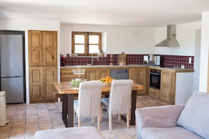 Eine Küche mit Holzschränken, einem Esstisch mit Stühlen, einem eingebauten Backofen und einem Fenster über der Spüle.