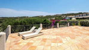 Una terraza en la azotea con suelo de baldosas, barandilla de metal y dos sillones de relax.