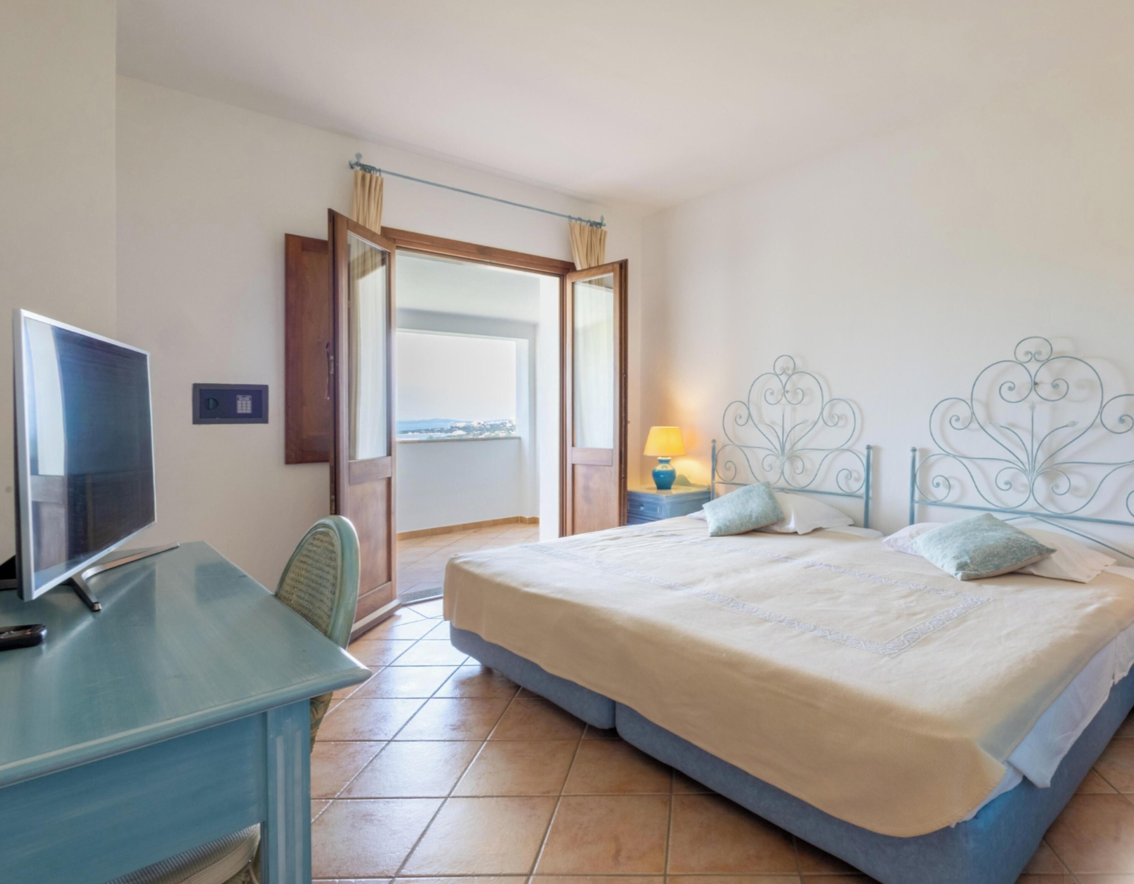 Habitación de hotel con cama, escritorio con televisor, ventana con vista y puerta que da a un área exterior.