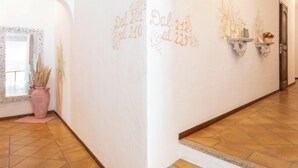 A hallway with white walls, a tiled floor, and a staircase leading to another level. There are decorative wall sconces and a potted plant. - Hotiday Baja Sardinia Saline (Baja Sardinia)