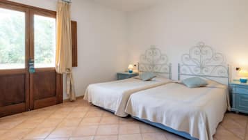 Una cama doble con cabecera metálica, una mesita de noche con lámpara y vista al exterior por una puerta corrediza.