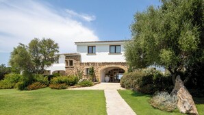 A two-story house with a stone facade, a central archway, and a well-maintained lawn. - Hotiday Baja Sardinia Saline (Baja Sardinia)