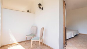 A room with two chairs, a wall-mounted light fixture, and a bed in the background. - Hotiday Baja Sardinia Saline (Baja Sardinia)