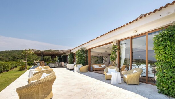An outdoor patio area with wicker furniture, a stone floor, and a view of the surrounding landscape. - Hotiday Baja Sardinia Saline (Baja Sardinia)