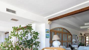 A spacious living area with wicker furniture, a large potted plant, and a view of the outside.