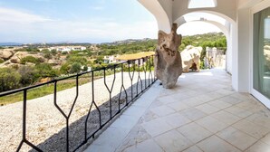 A balcony with a stone sculpture, white walls, and a view of a coastal landscape. - Hotiday Baja Sardinia Saline (Baja Sardinia)