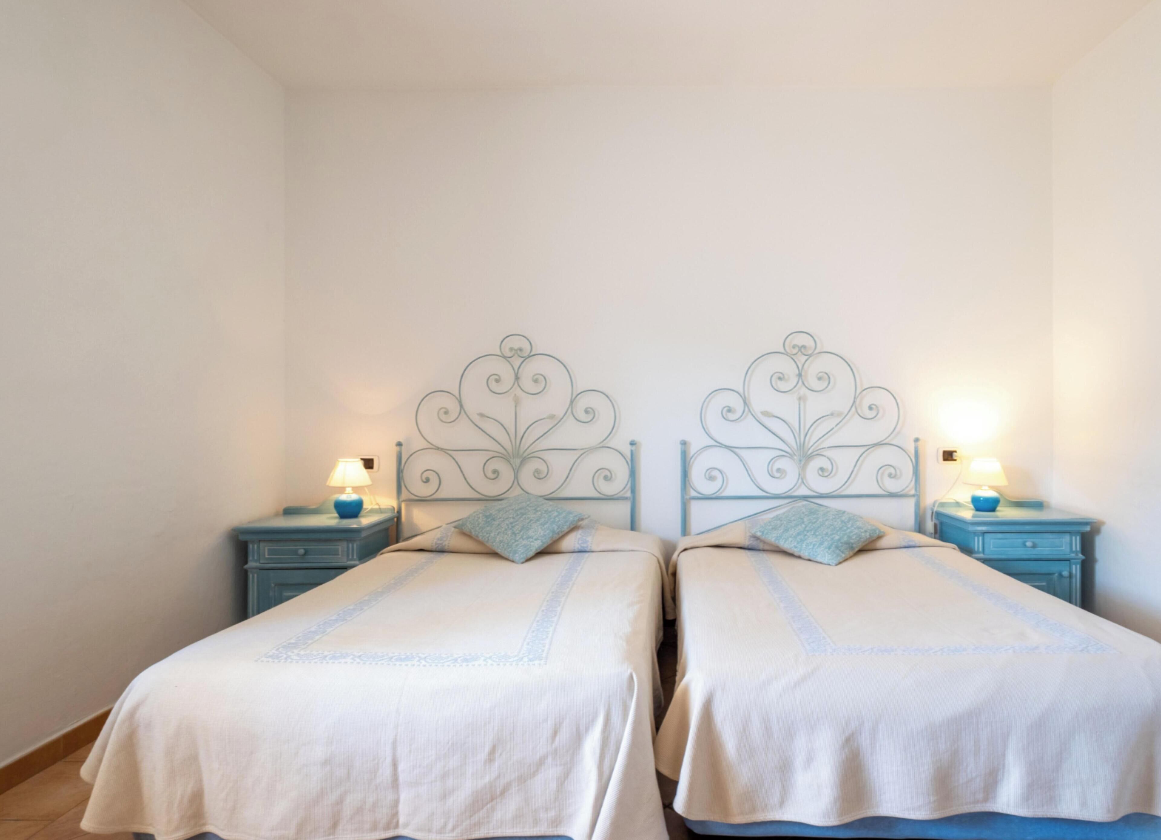 A double room with two beds, each with a metal headboard, and bedside tables with lamps.