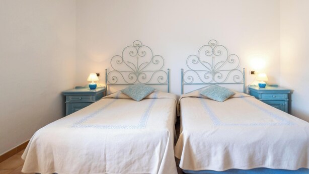 A double room with two beds, each with a metal headboard, and bedside tables with lamps. - Hotiday Baja Sardinia Saline (Baja Sardinia)