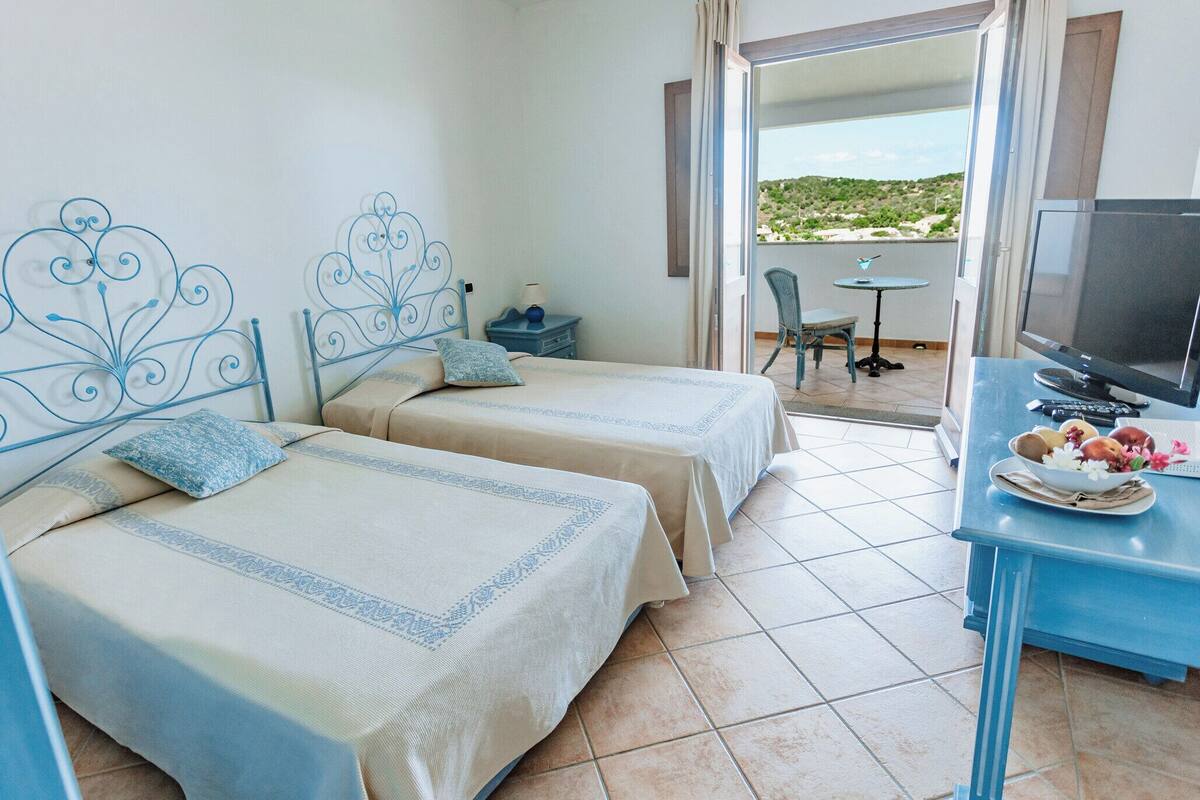 Habitación de hotel con dos camas, televisión, una mesita con frutero y balcón con vistas.