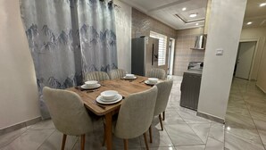 A dining area with a wooden table set for six, surrounded by six chairs. - Prime Apartment Dalaba (Old-Yundum)
