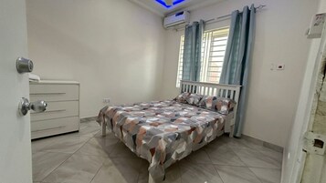 Un dormitorio con cama, cómoda, ventana con cortinas y equipo de aire acondicionado.