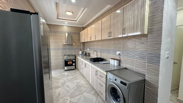 A modern kitchen with stainless steel appliances, a built-in oven, and a washing machine. - Prime Apartment Dalaba (Old-Yundum)