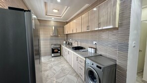 A modern kitchen with stainless steel appliances, a built-in oven, and a washing machine. - Prime Apartment Dalaba (Old-Yundum)