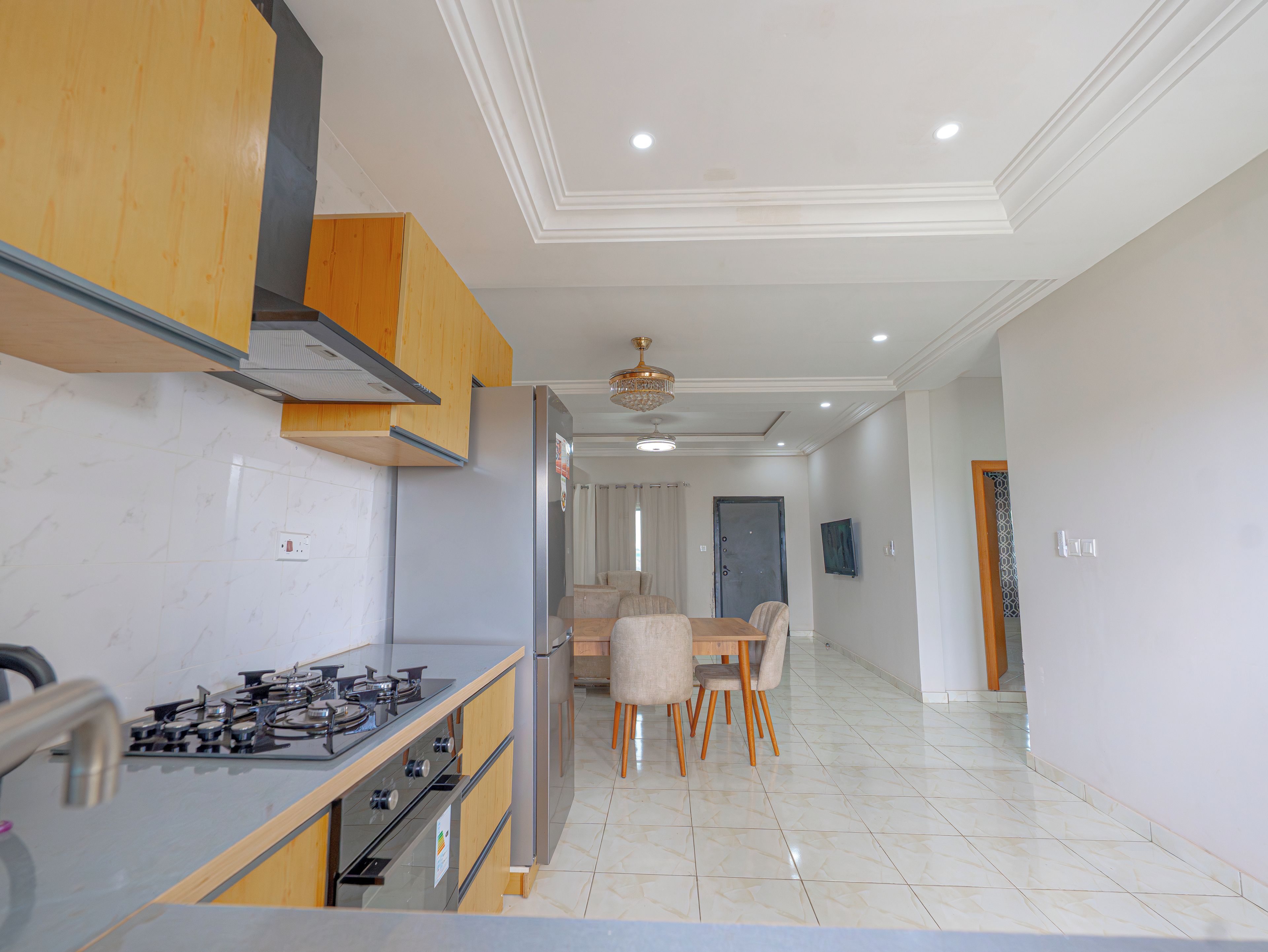 A modern kitchen with a gas stove, stainless steel appliances, wooden cabinets, and a dining area with a table and chairs.