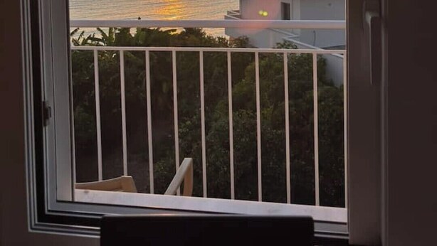 Un balcó amb vista al capvespre sobre la mar, un edifici al fons i una barana.