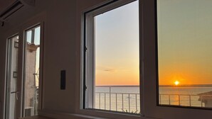 Habitació amb vista al capvespre sobre la mar, un portàtil damunt d'una taula i una finestra que també domina la mar.