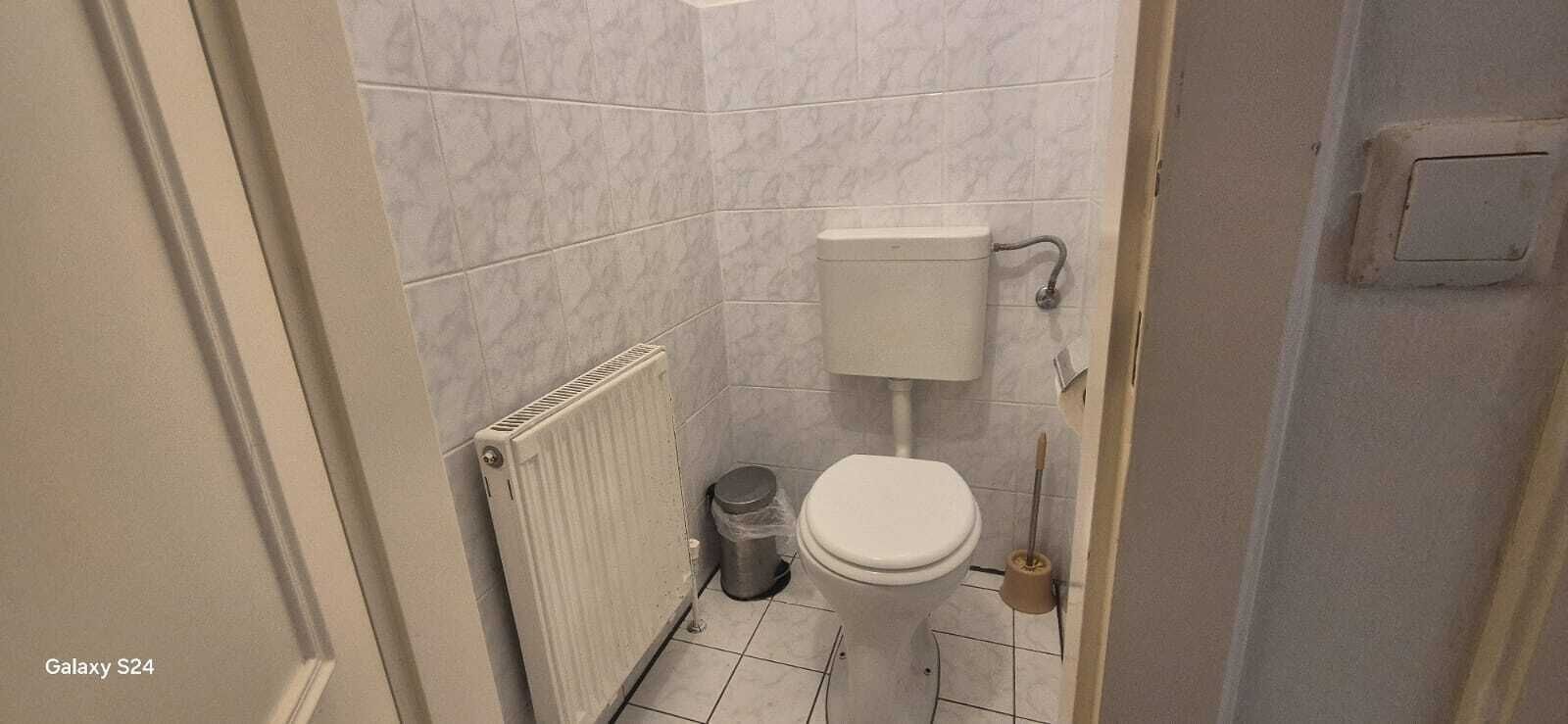 A small bathroom with a toilet, a radiator, and a trash bin.