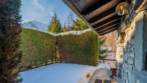 A snow-covered courtyard with a stone wall, wooden beams, and a bench.