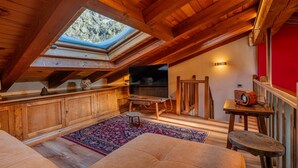 An attic room with a wooden ceiling, a skylight, a television, a red wall, and a patterned rug.