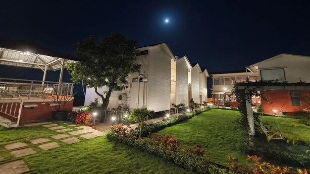 A modern building with a well-lit exterior, a paved pathway, and a small lawn area. - Rhythm Eco And Agro Stays (Mahabaleshwar)