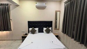 A bedroom with a bed, a ceiling fan, a nightstand, a mirror, and curtains. - Hotel Stay Inn Rabale (Navi Mumbai)