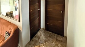 A hallway with two dark wooden doors, a brown leather sofa, and a mirror reflecting a person outside. - Hotel Stay Inn Rabale (Navi Mumbai)