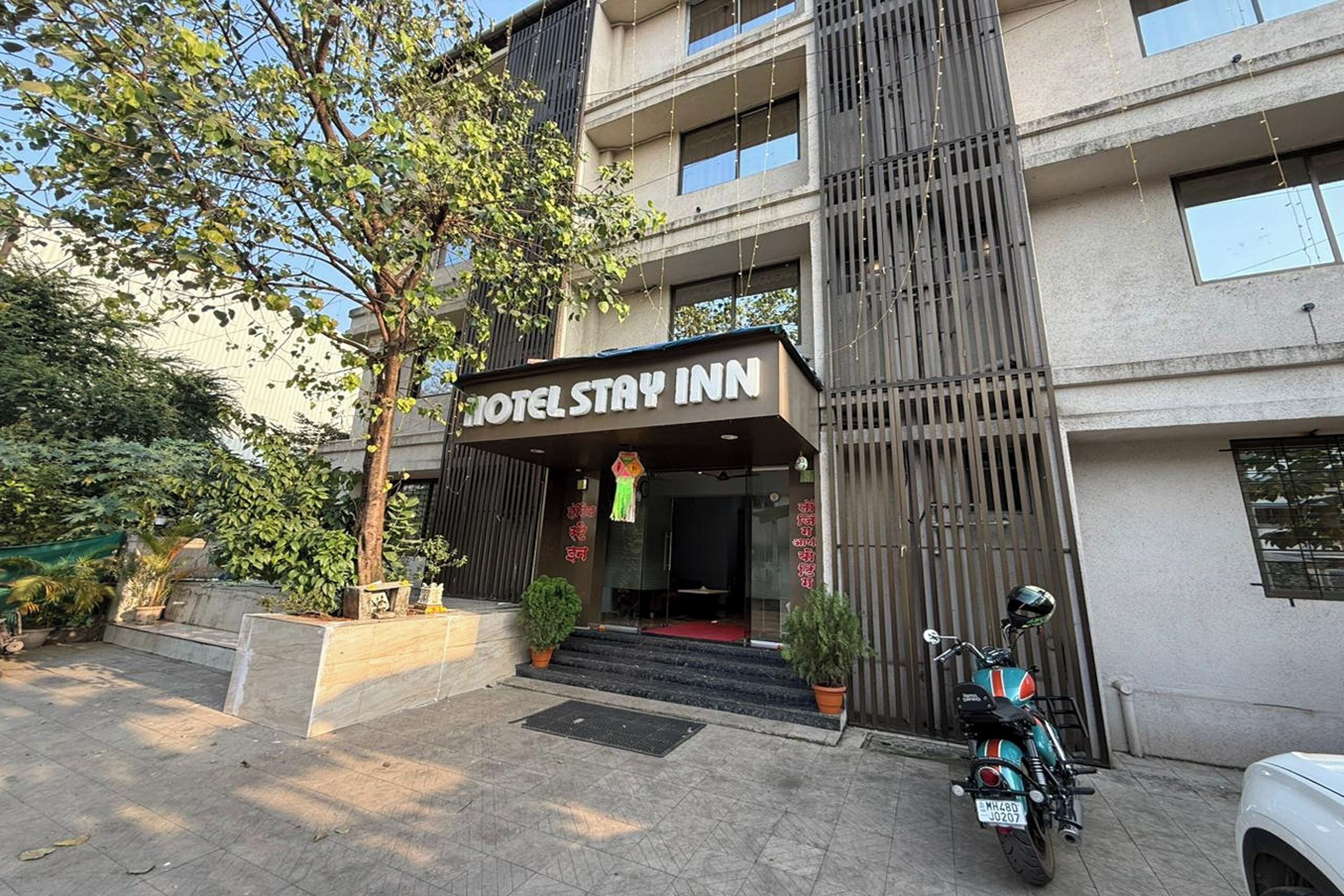 A hotel entrance with a sign reading "HOTEL STAY INN," steps leading up to the entrance, a motorcycle parked in front, and a tree to the left.