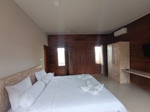 A hotel room with a large bed, wooden walls, a TV mounted on the wall, and a window with curtains. - Saghara Villa Amed (Karangasem)