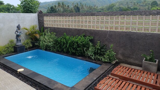 A swimming pool with a statue, surrounded by plants and a view of a mountainous landscape. - Saghara Villa Amed (Karangasem)